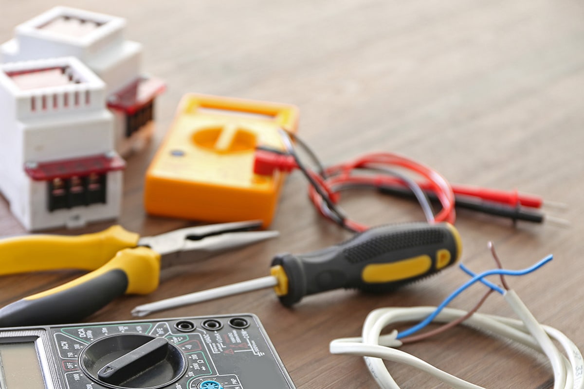 Outils d'électricien posés sur un plan de travail : multimètre, pince, tournevis et câble