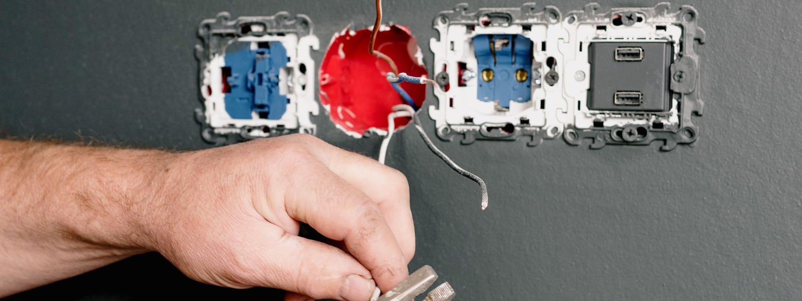 Électricien remplaçant à la pince un appareillage encastré dans le mur
